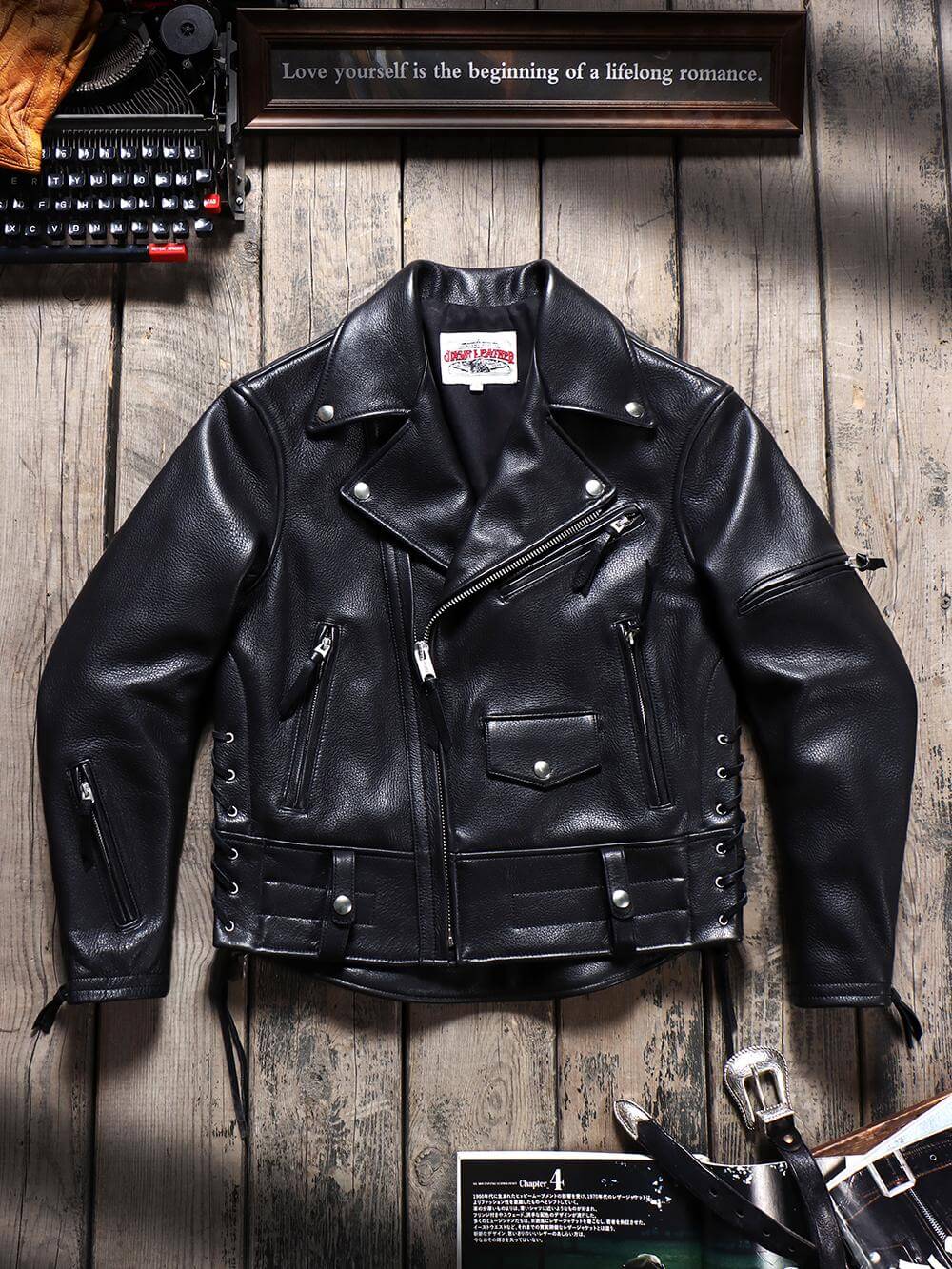 Black leather jacket on a wooden surface with a typewriter and motivational quote in the background.