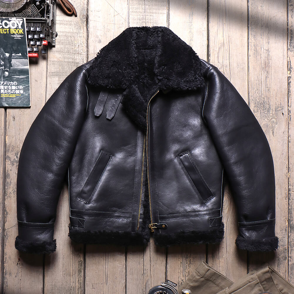 A black leather aviator-style jacket with a thick black shearling collar and lining, laid flat on a rustic wooden plank background.